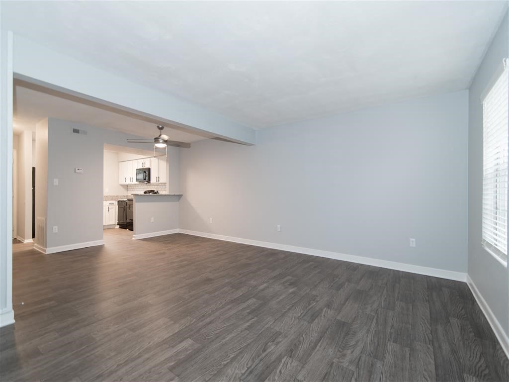 an empty living room with wood floors and a kitchen