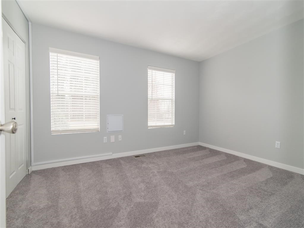 an empty room with carpet and two windows