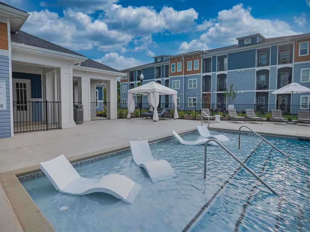 a swimming pool with white chairs and umbrellas in front of apartment buildings