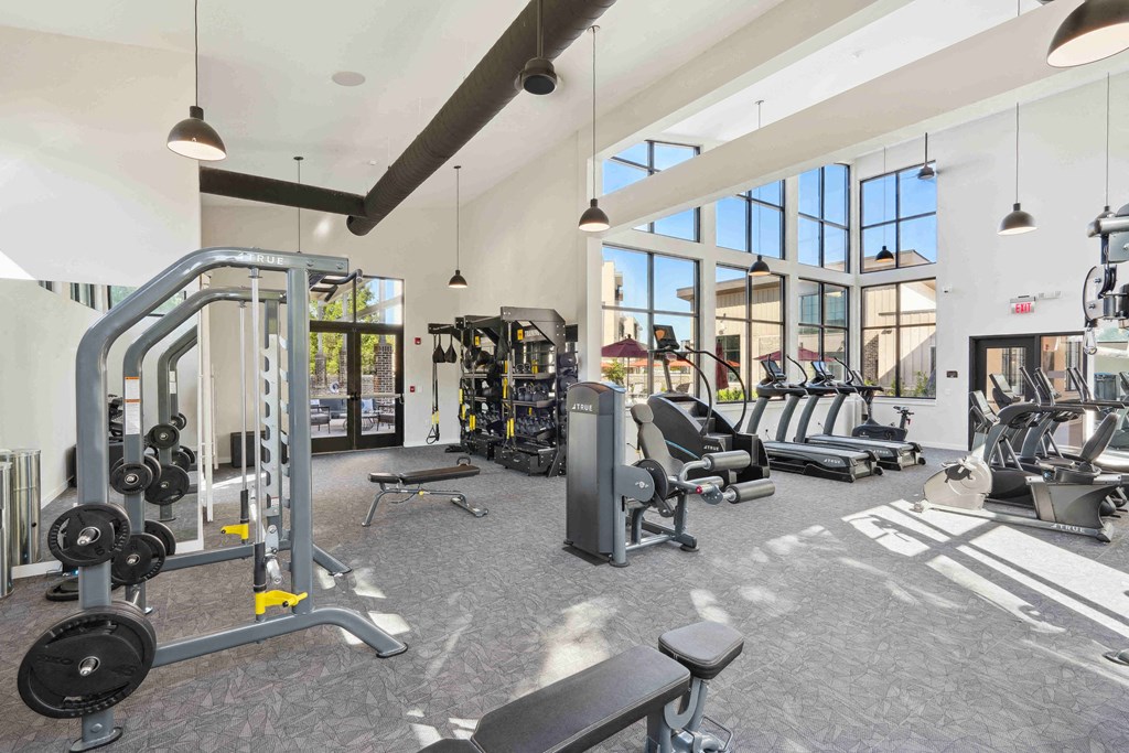 a gym with weights and cardio equipment in a building with large windows