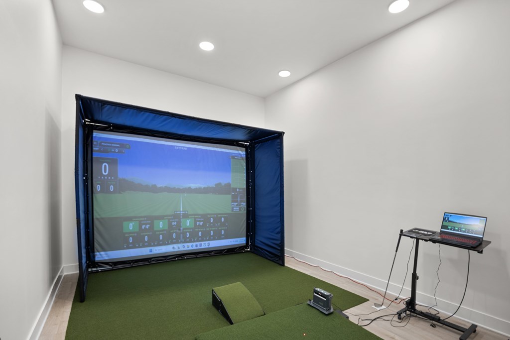 Golf simulator room with a large screen and a laptop on a table.