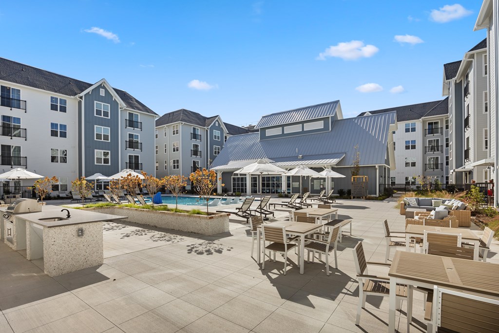 Outdoor seating area with tables and umbrellas next to the pool.