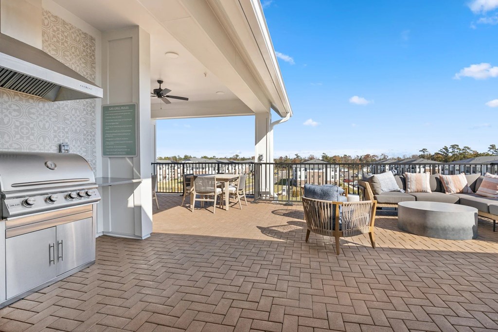 A Patio with a Grill and Chairs Overlooking a Fence.