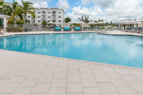 A large swimming pool surrounded by a white tiled floor and a white building in the background.