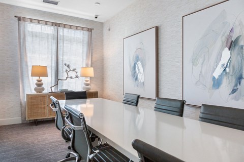 A conference room with a long table, chairs, and two paintings on the wall.