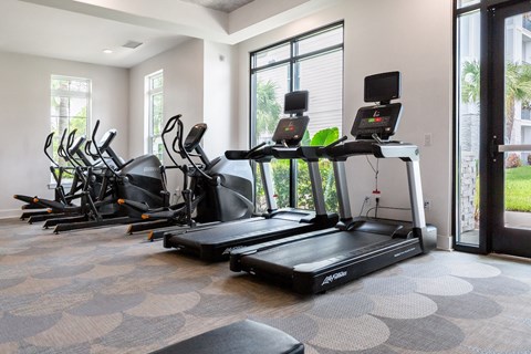 A treadmill and elliptical machines are in a spacious gym.