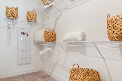 A white shelf with baskets and a white pillow.