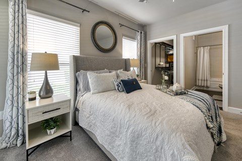 A bedroom with a large bed, a nightstand with a lamp, and a mirror on the wall.
