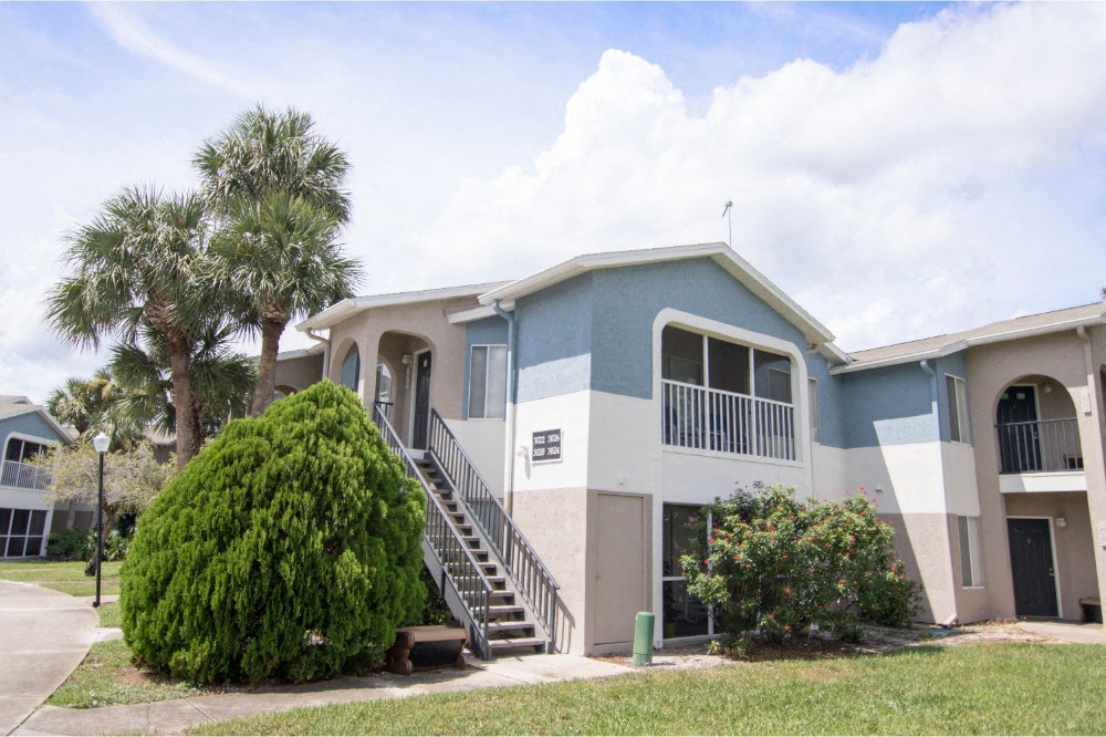 The building exterior of Park Village- two stories showing staircase, landscaping, and balcony
