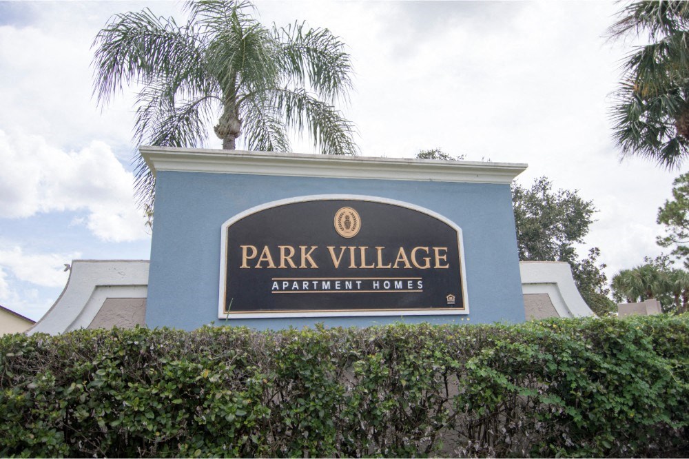 The main sign at Park Village- sign reads "Park Village Apartment Homes"- blue sign
