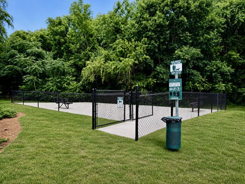 A signpost stands in a grassy area with a trash can and a fence in the background.