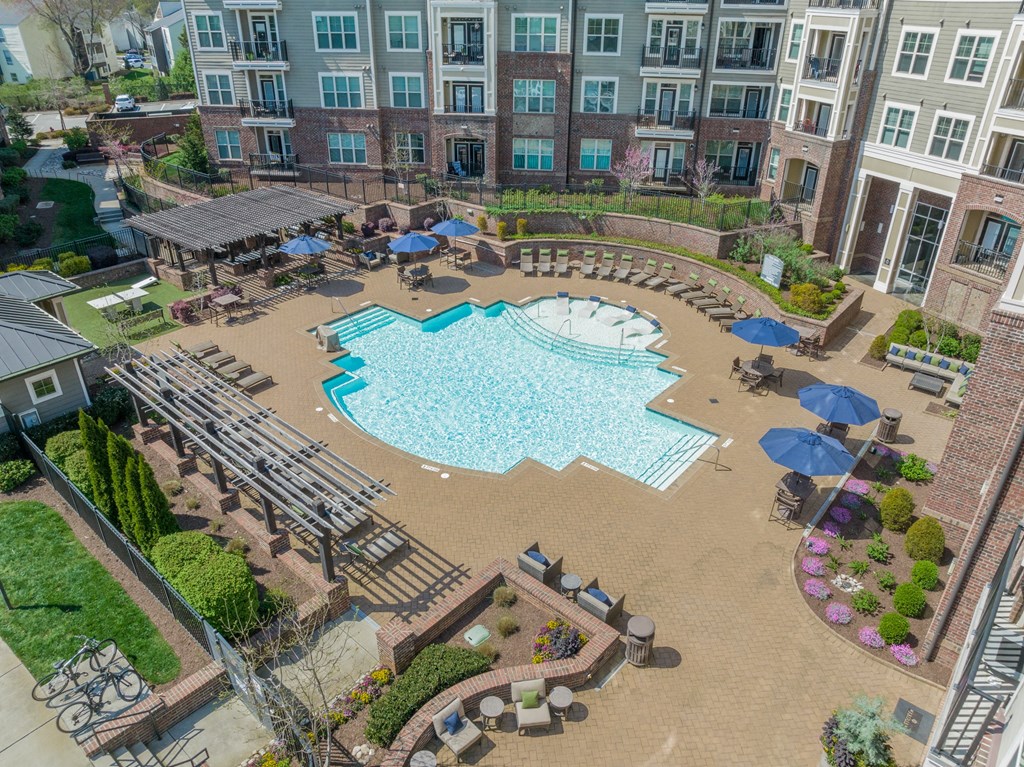 a large swimming pool with lounge chairs and umbrellas in front of an apartment building