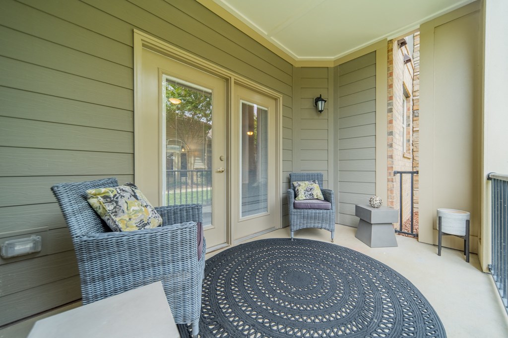 a covered porch with two chairs and a rug