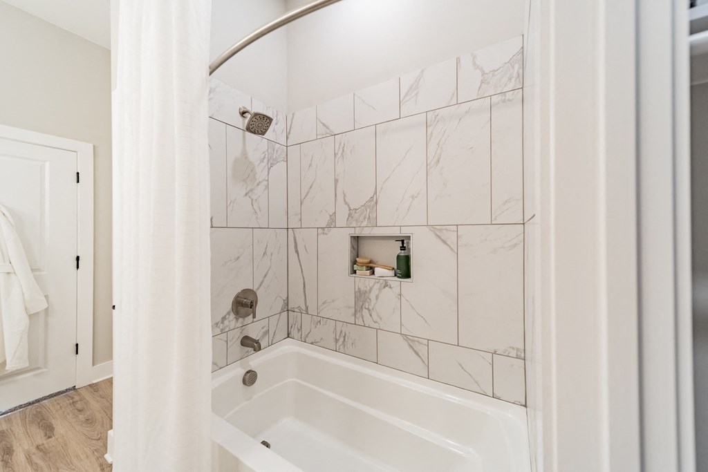 A white bathroom with a marble tile wall and a white tub.