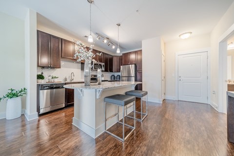 a kitchen with a large island with stools and a stainless steel refrigerator