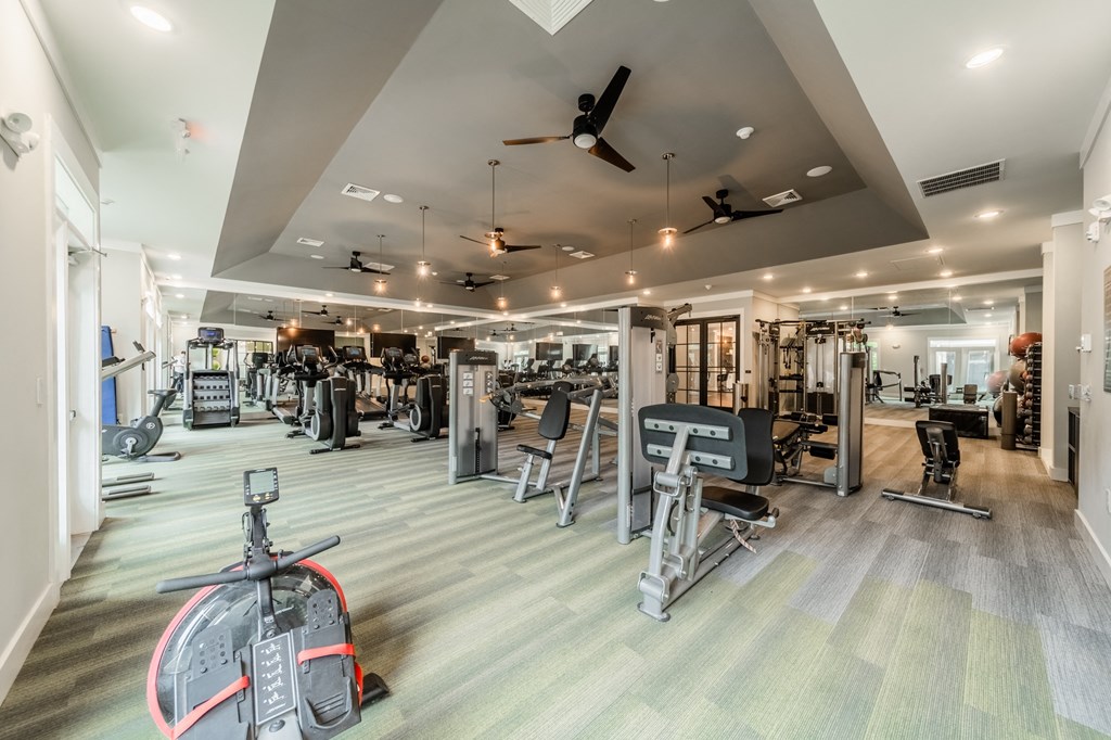 a gym with cardio machines and weights on the floor and a ceiling fan