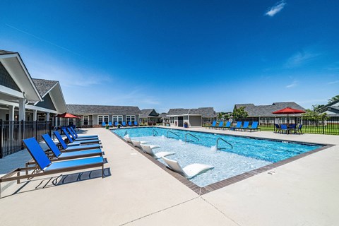 A swimming pool with blue lounge chairs and a red roofed building in the background.