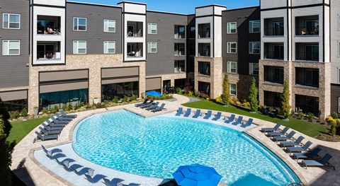 A large swimming pool surrounded by lounge chairs in front of apartment buildings at Liam at Hays Farm in Huntsville, Alabama
