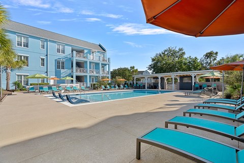 A sunny day at the pool with blue lounge chairs and a white building in the background.