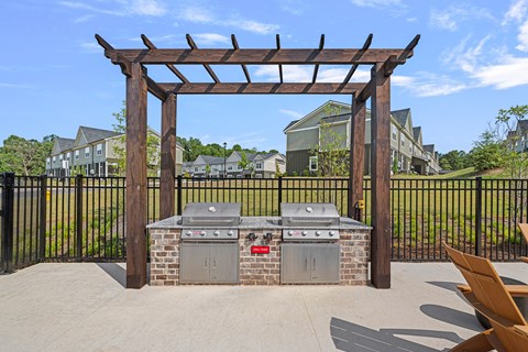 A BBQ grill is under a wooden pergola in a backyard.
