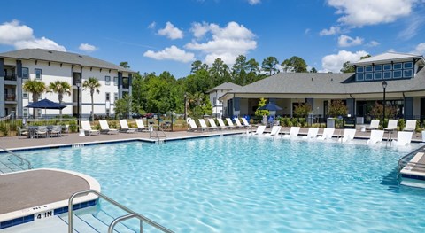 A large swimming pool with lounge chairs and a building in the background at Crossings at Pooler Apartments in Pooler, GA