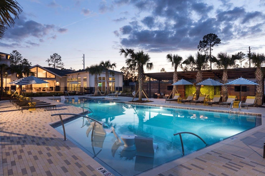 a large swimming pool with chairs and umbrellas at dusk