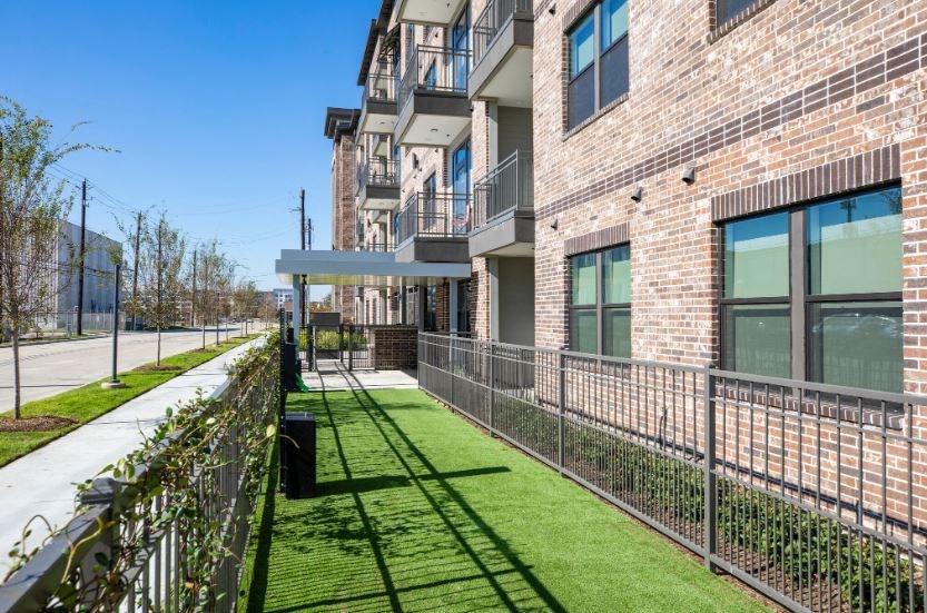 a grassy area with a fence in front of a brick building