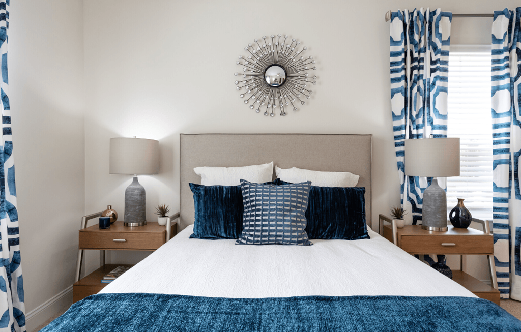 a bedroom with a bed and blue and white pillows and a sunburst mirror