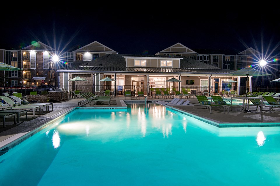 a swimming pool at night with chairs and a building in the background