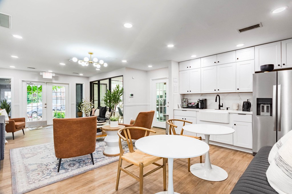 a living room with tables and chairs and a kitchen with white cabinets