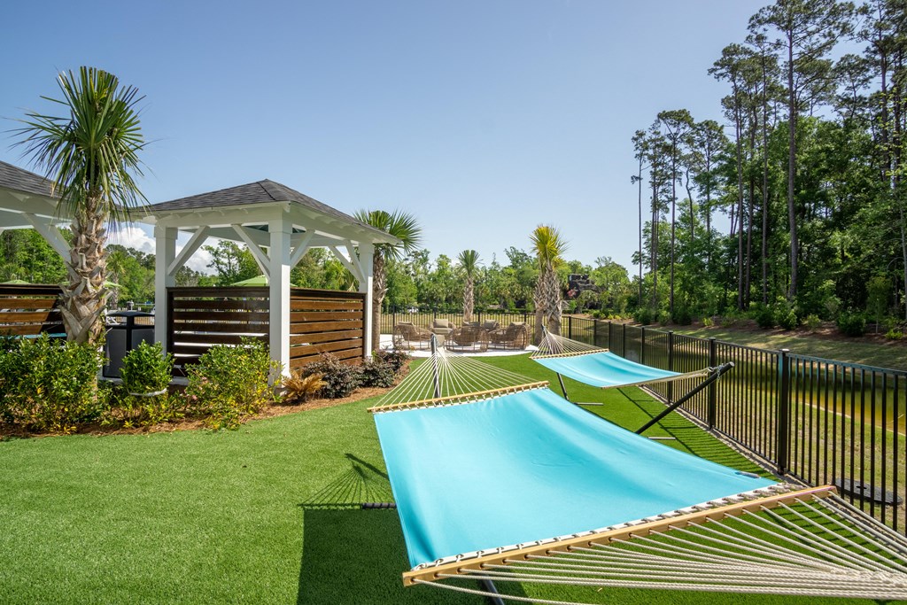 a row of hammocks in a backyard with a pool and gazebo