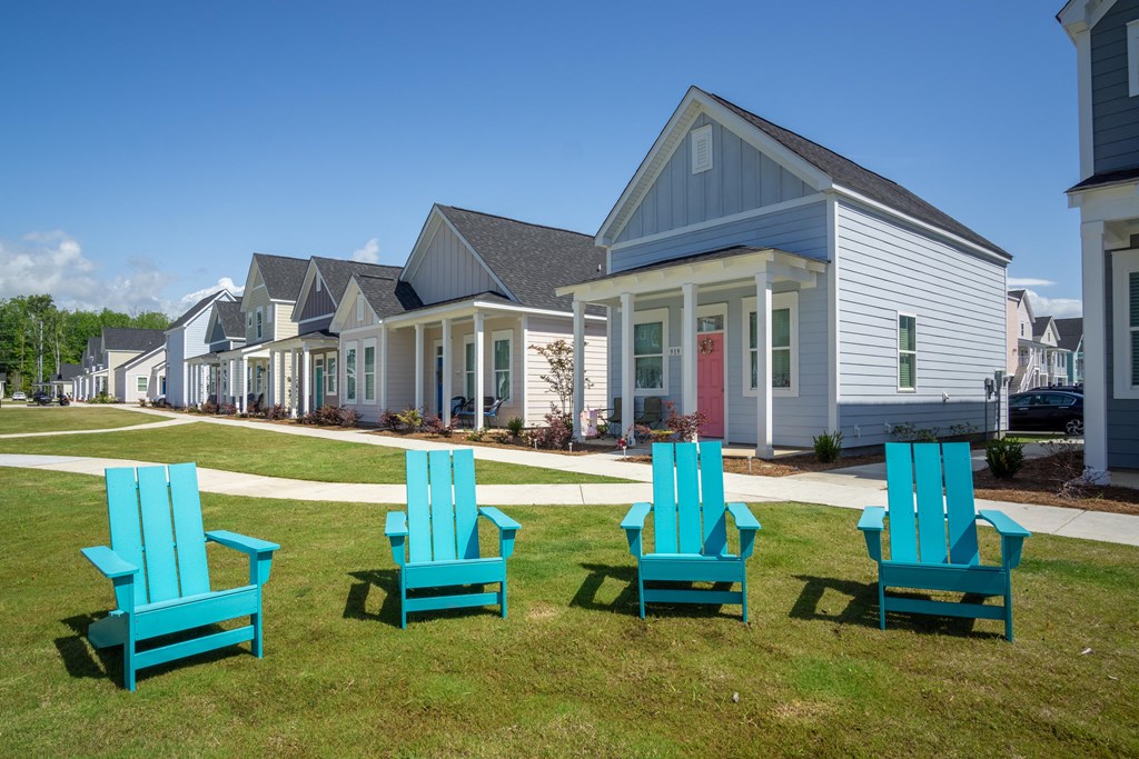 four blue adirondack chairs in front of a row of houses