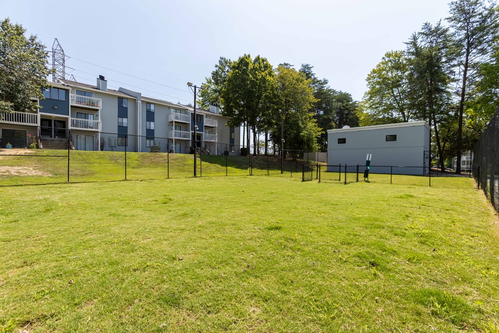 A dog park with a building and trees in the background at Enclave at 38 Twenty Two Apartments in Greensboro, NC
