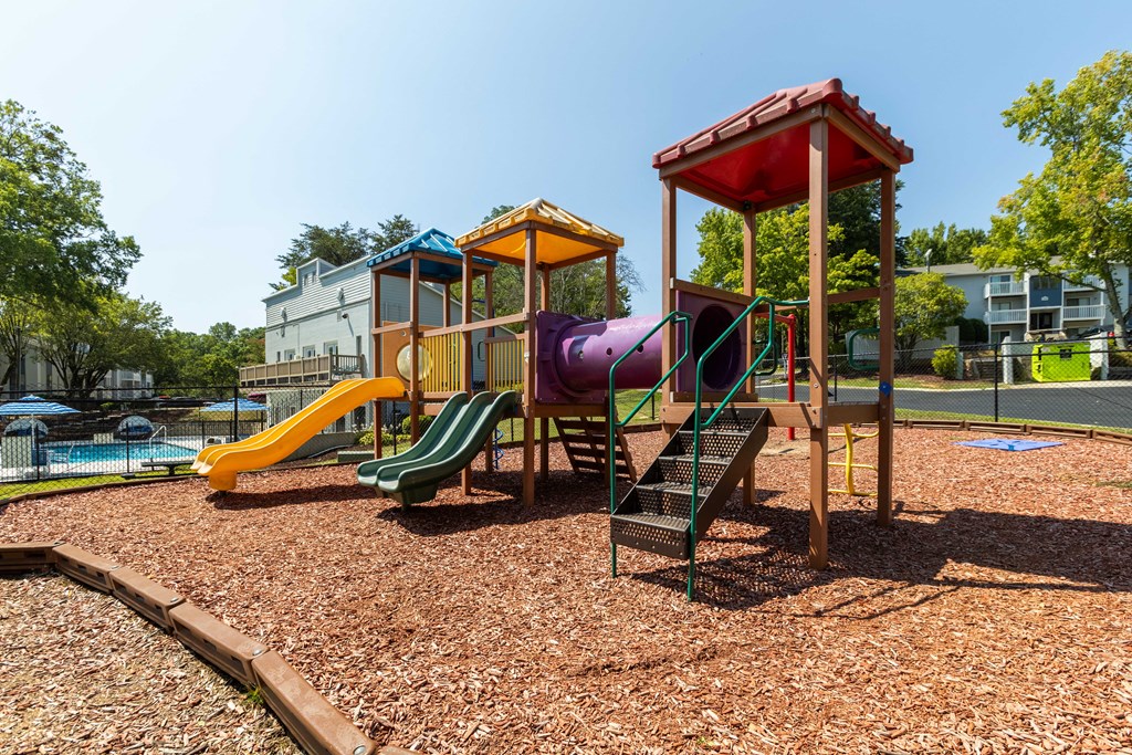A playground with a yellow slide, a purple slide, and a red and yellow playhouse at Enclave at 38 Twenty Two Apartments in Greensboro, NC