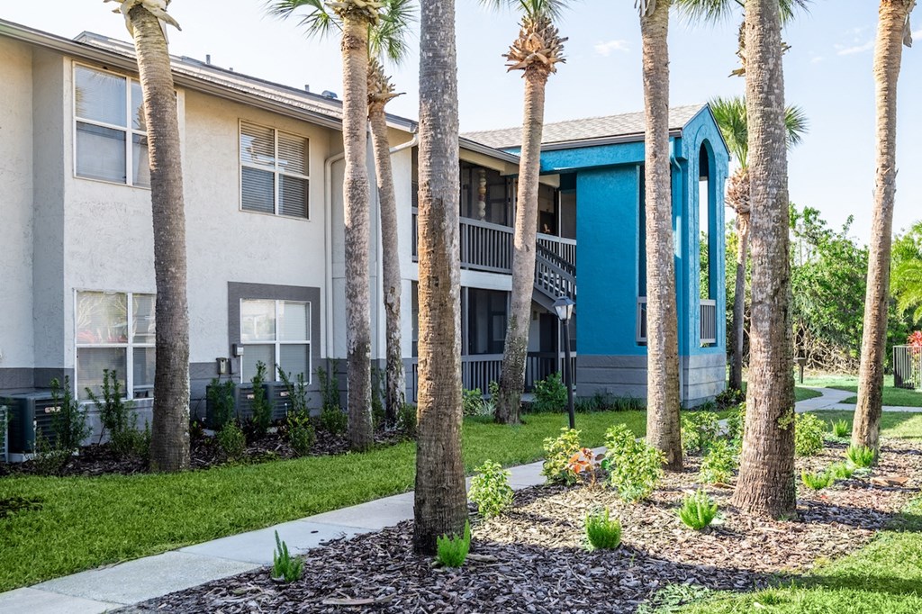 a building with a blue and white exterior and a sidewalk and palm trees in front of it