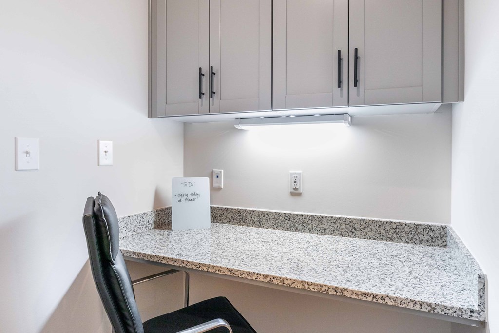 a kitchen with white cabinets and a granite counter top with a desk and a chair