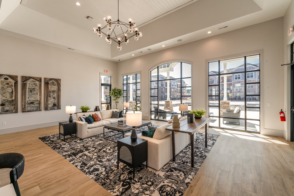 A well-lit, modern living room with a large rug, a sofa set, a coffee table, and a chandelier.
