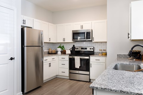 A kitchen with a refrigerator, microwave, oven, and sink.