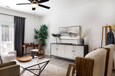 A living room with a ceiling fan, a chair, a table, a cabinet, and a painting on the wall.
