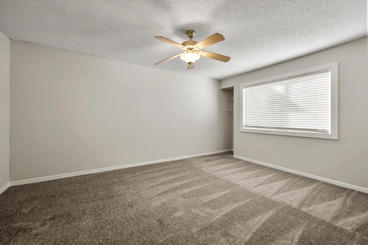 an empty bedroom with a ceiling fan and a window