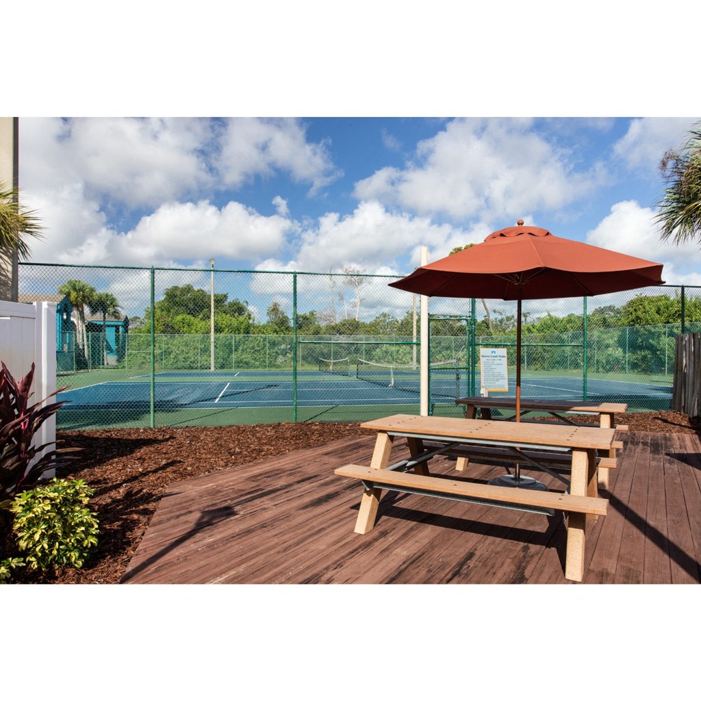 a picnic table with an umbrella next to a tennis court