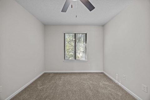 A bedroom painted white with a ceiling fan and a window with blinds.