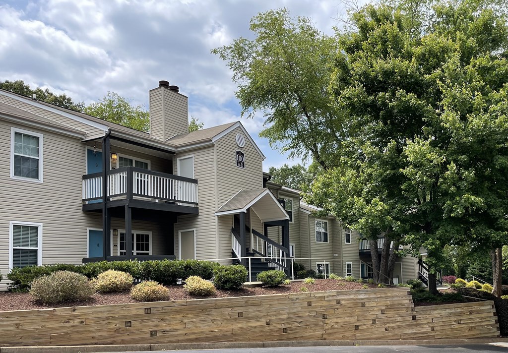 an exterior view of an apartment complex with a stone retaining wall and trees