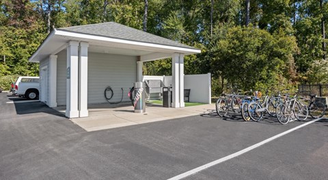 A small white building with a grey roof is surrounded by a parking lot with bicycles parked in front.