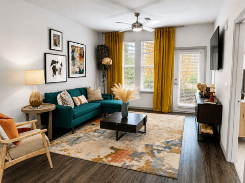 A living room with a green couch, a wooden chair, a coffee table, and a rug.