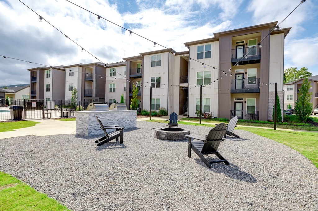 an outdoor area with a fire pit and chairs in front of an apartment building