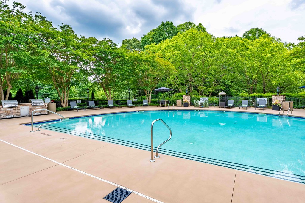 a swimming pool with chairs around it and trees in the background
