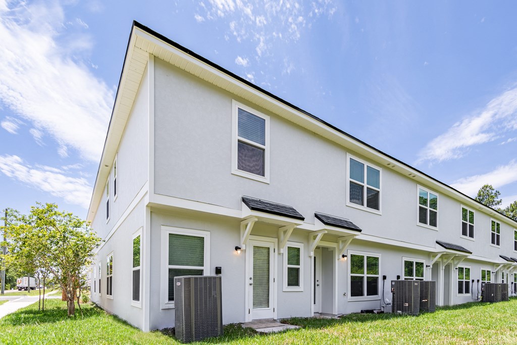 the exterior of a white house with green grass and a blue sky