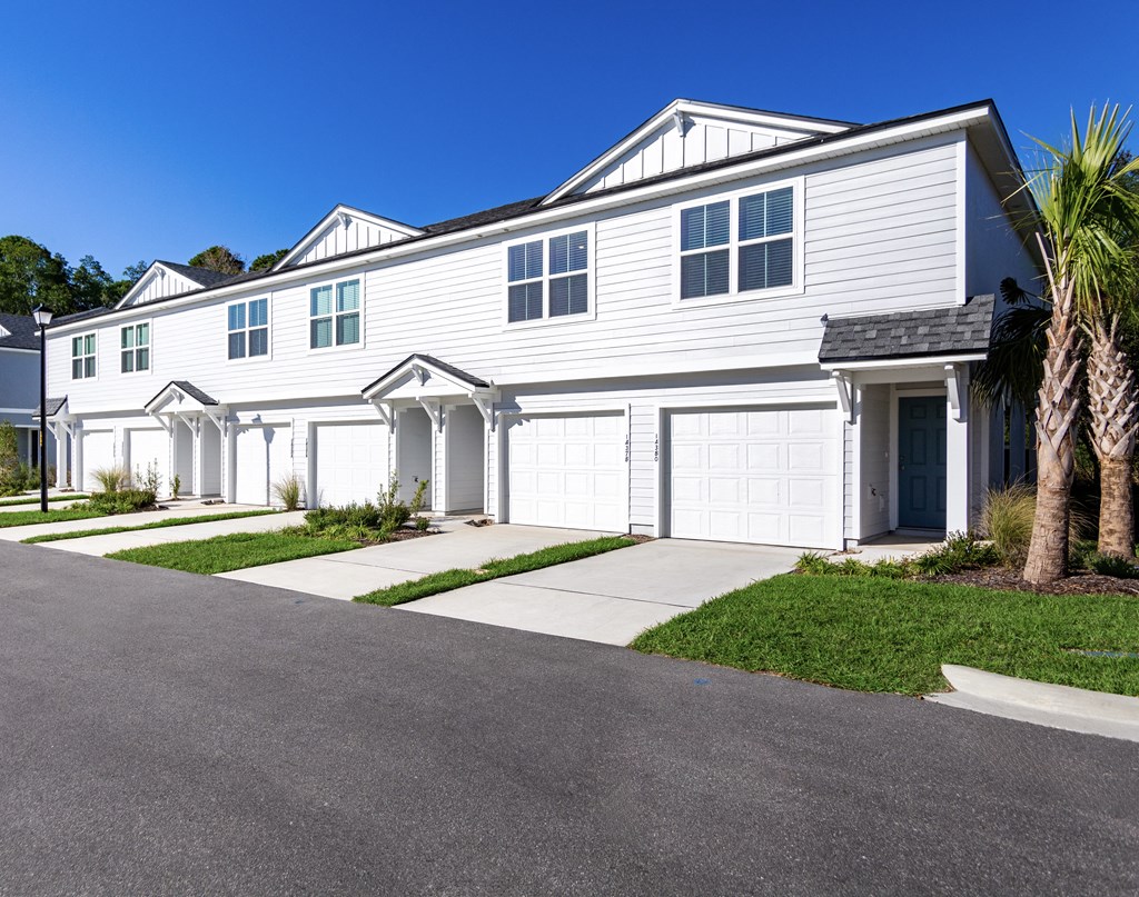 A white house with a grey roof and a palm tree in front.