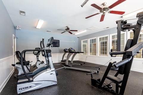 A home gym with a treadmill, elliptical trainer, and a fan.